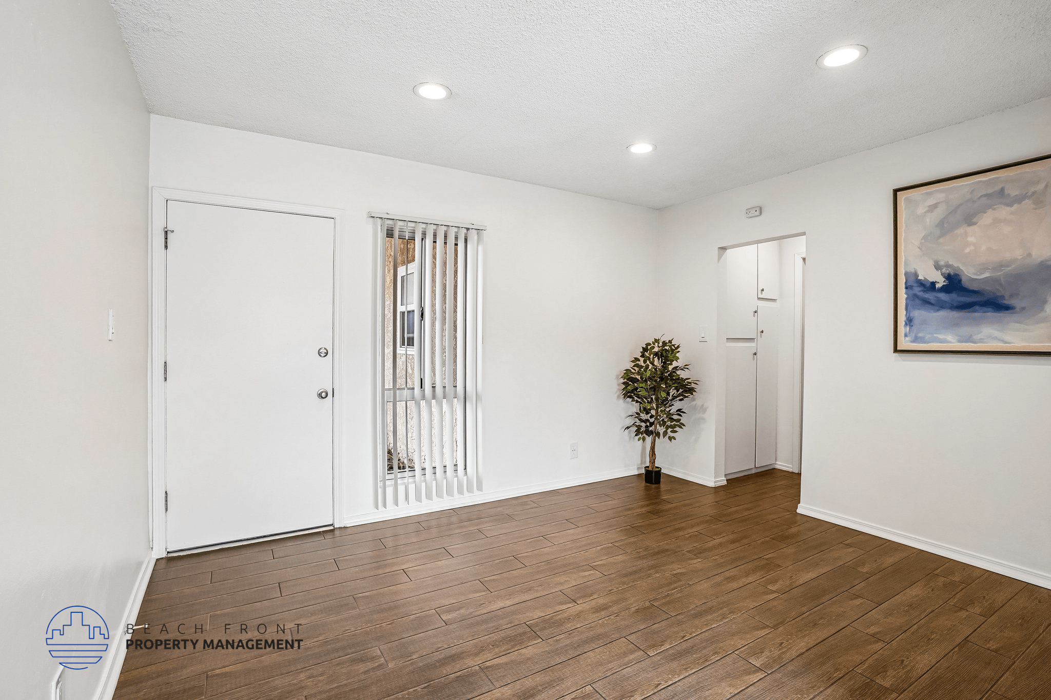 A room with a wooden floor and white walls, with a door on the left and a painting on the right.